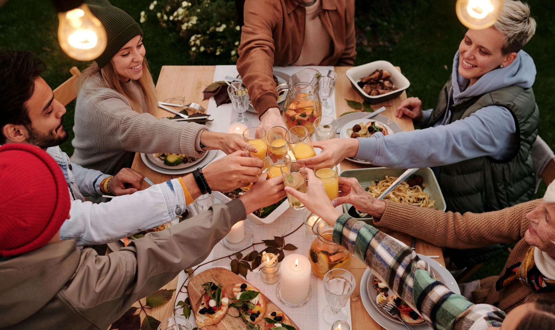 Group of friends toasting with glasses at an outdoor dinner table. Lively and joyful atmosphere.