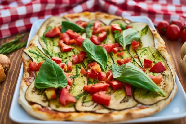 Close-up of a vibrant Italian pizza topped with fresh eggplant, basil, and tomatoes.